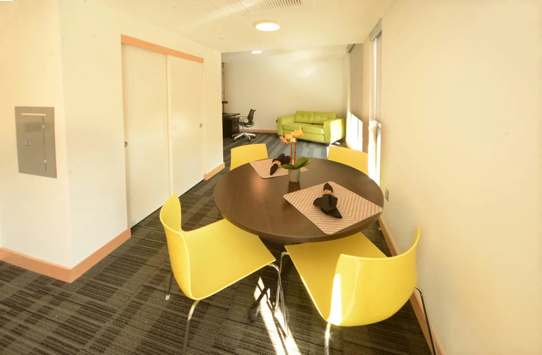 A dark brown round wood dining table with four yellow chairs in a carpeted hallway.