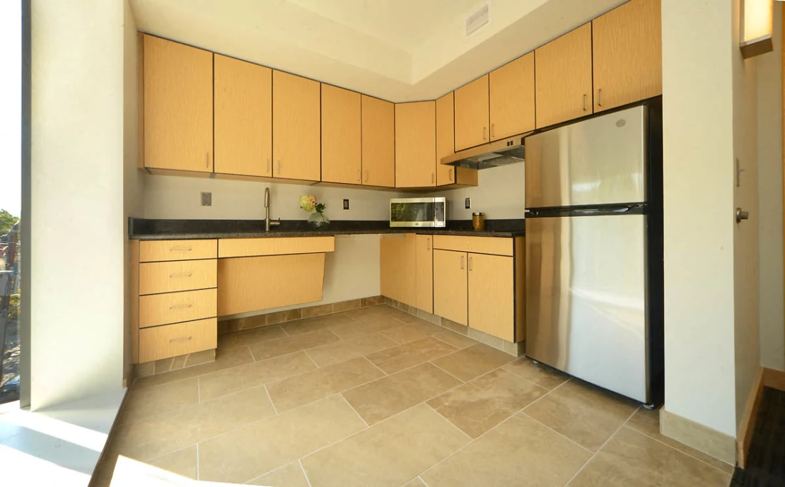 An open corner kitchen with a floor to ceiling window, beige cabinets, a stainless refrigerator, sink, stove with range hood, and a toaster oven.