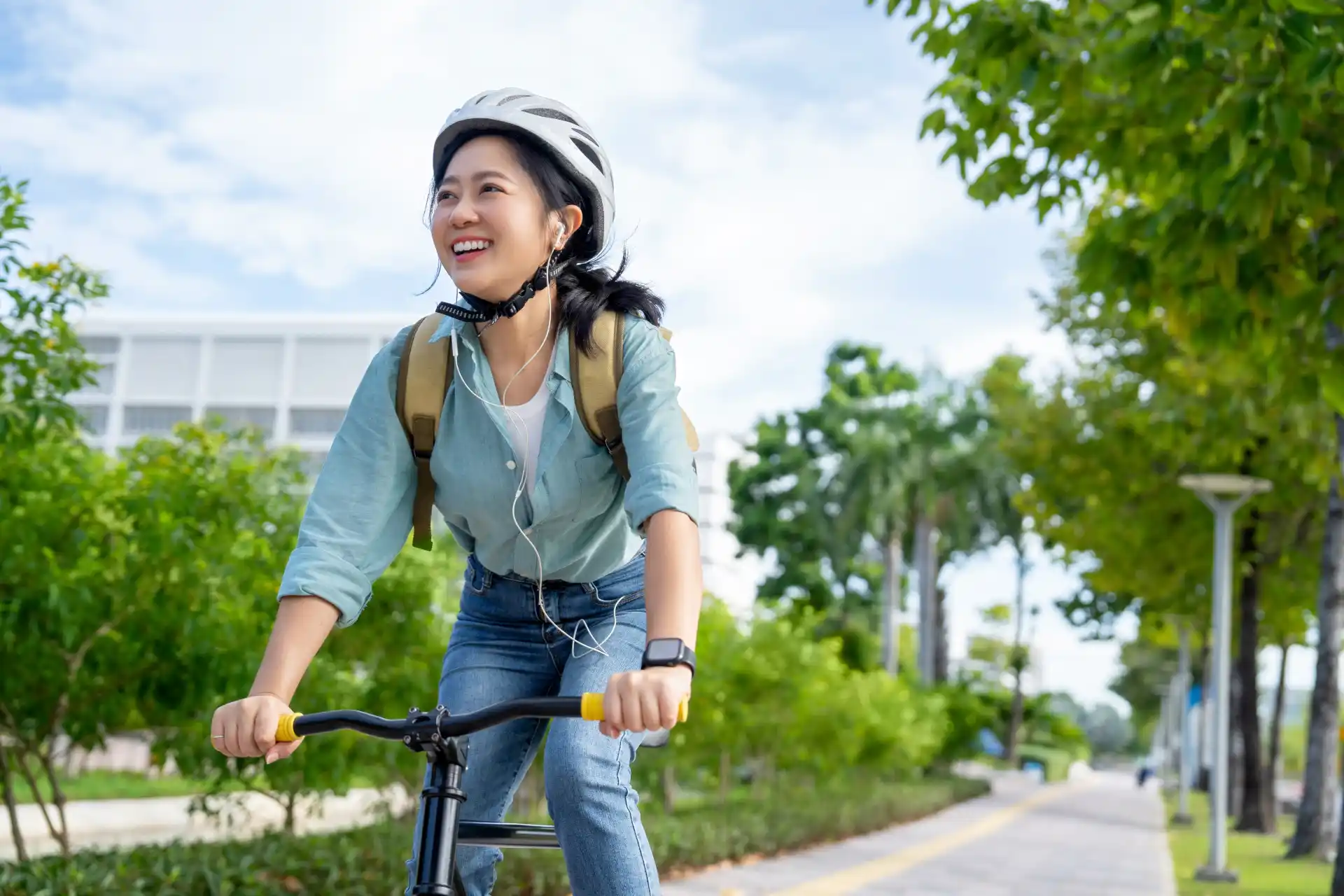 A young woman wearing a helmet and backpack smiles while riding a bike to campus on a sunny day.